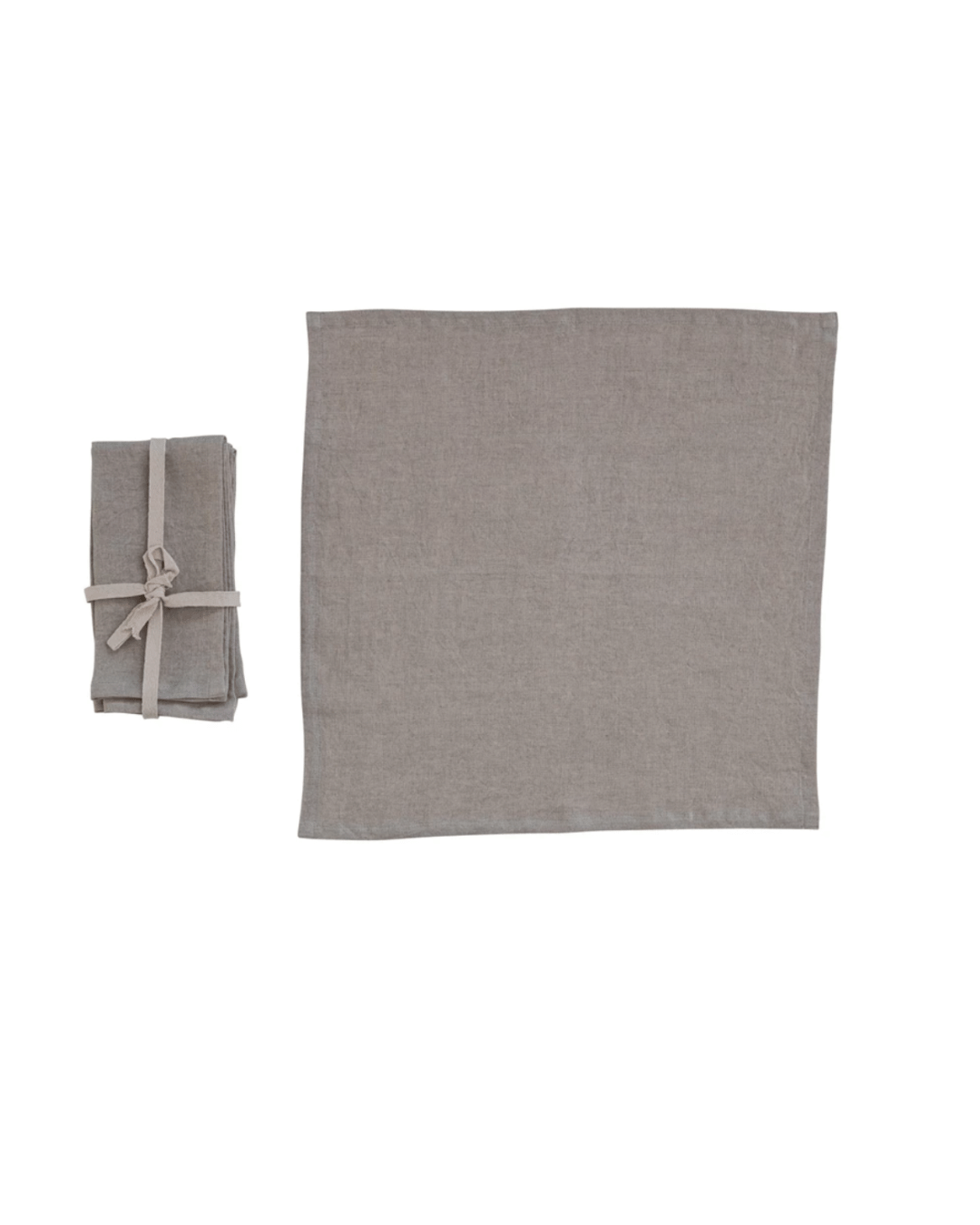 A large, unfolded piece of natural linen cloth is spread out flat. To its left sits a smaller stack of Creative Co-op's "Linen Napkins Grey S/4," neatly folded and secured with a matching beige ribbon against a plain white background.