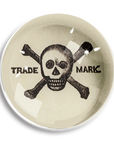 The Ben's Garden Dome Crystal Paperweight features a black skull and crossbones on an off-white background, with "TRADE" and "MARK" flanking it. Inspired by New York studio style, it evokes the charm of handcrafted French crystal.