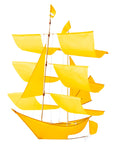 The Faire Sailing Ship Kite features multiple bright yellow sails and a brown mast, evoking a handmade aesthetic. Photographed on a white background.