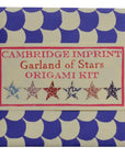 A square package with a blue and white scallop pattern features the "Origami Star Garland" by Faire. The label displays five patterned origami paper stars along the bottom in different designs.