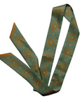 The Faire Twilly Scarf features green silk with orange starburst and diamond patterns, a small horseshoe design, pointed ends, and a gold-toned reverse—making it the perfect gift for any special occasion.