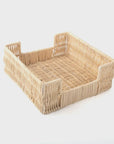 The Rattan Bev Napkin Tray by Faire is a square, handcrafted wicker basket featuring slightly raised sides and an open-top design, making it a charming holder for cocktail napkins. Made from natural rattan, its light beige hue contrasts beautifully against a plain white background.