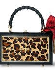 The Faire Leopard Supreme Bag features a rectangular leopard print cowhide design with a black frame, gold accents, and black bamboo handle. It’s finished with a bold red bow, beige tassel, four gold feet, and an eye-catching gold leopard bauble.