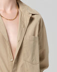 A person wears the Kayla Shirt Catalina by Citizens Of Humanity/AGOLDE, an open beige cotton poplin shirt, and a gold chain necklace, shown from shoulders to mid-chest against a plain light background.