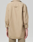 Model shown from the back wearing the Kayla Shirt Catalina by Citizens Of Humanity/AGOLDE—a loose-fitting, beige, long-sleeve poplin shirt with rolled sleeves—paired with beige pants against a plain gray background.
