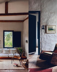 A cozy living room with rustic white walls, wooden beams, and a white sofa exudes charm inspired by Nina Freudenberger’s "Mountain House" from Random House, blending inviting design with scenic views reminiscent of mountain retreats.