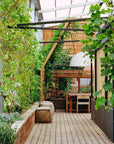 Discover nature-inspired decor with "Outside In: Thoughtful Interiors" by Random House, featuring cozy wood floors, green vines on trellises, cushioned benches, and sunlit tables beneath a glass roof for beautiful homes.