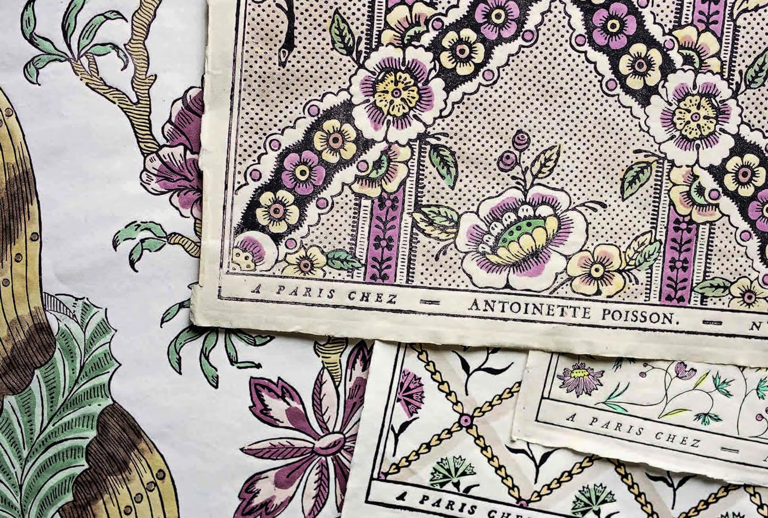 Close-up of vintage-style domino paper from "A Year in the French Style" by Random House, featuring pink, green, and yellow floral patterns and overlapping sheets that reflect classic French design.