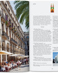 An open book—New York Times 36 Hours Europe by Ingram Book Company—shows people dining by a grand building in a sunny plaza; the other page offers Barcelona tips, colorful glass, and a modern building.