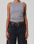 Wearing the Isabel Rib Tank by Citizens Of Humanity/AGOLDE, a person layers this gray racerback with high-waisted black jeans and a sleek black belt. Their arms rest relaxed by their sides against a neutral backdrop.