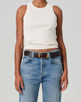 Someone is wearing an Isabel Rib Tank by Citizens Of Humanity/AGOLDE in crisp white, paired with light blue jeans and a dark brown belt with a gold buckle, standing against a plain background.