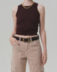 A person wears the Isabel Rib Tank F25 by Citizens Of Humanity/AGOLDE—a sleeveless, high-neck dark burgundy ribbed top—paired with beige cargo pants, a black belt with gold buckle, gold chain necklace, and rings. Their face is not visible.
