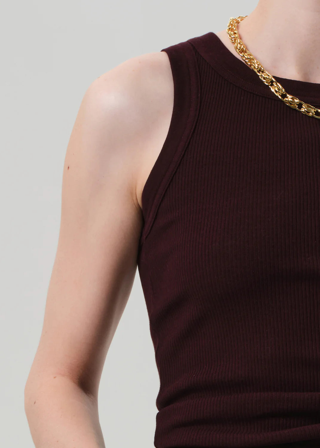 A model wears the Isabel Rib Tank F25 by Citizens Of Humanity/AGOLDE—a sleeveless, high neckline, ribbed dark burgundy top crafted from supportive cotton—paired with a chunky gold chain necklace against a light gray background.