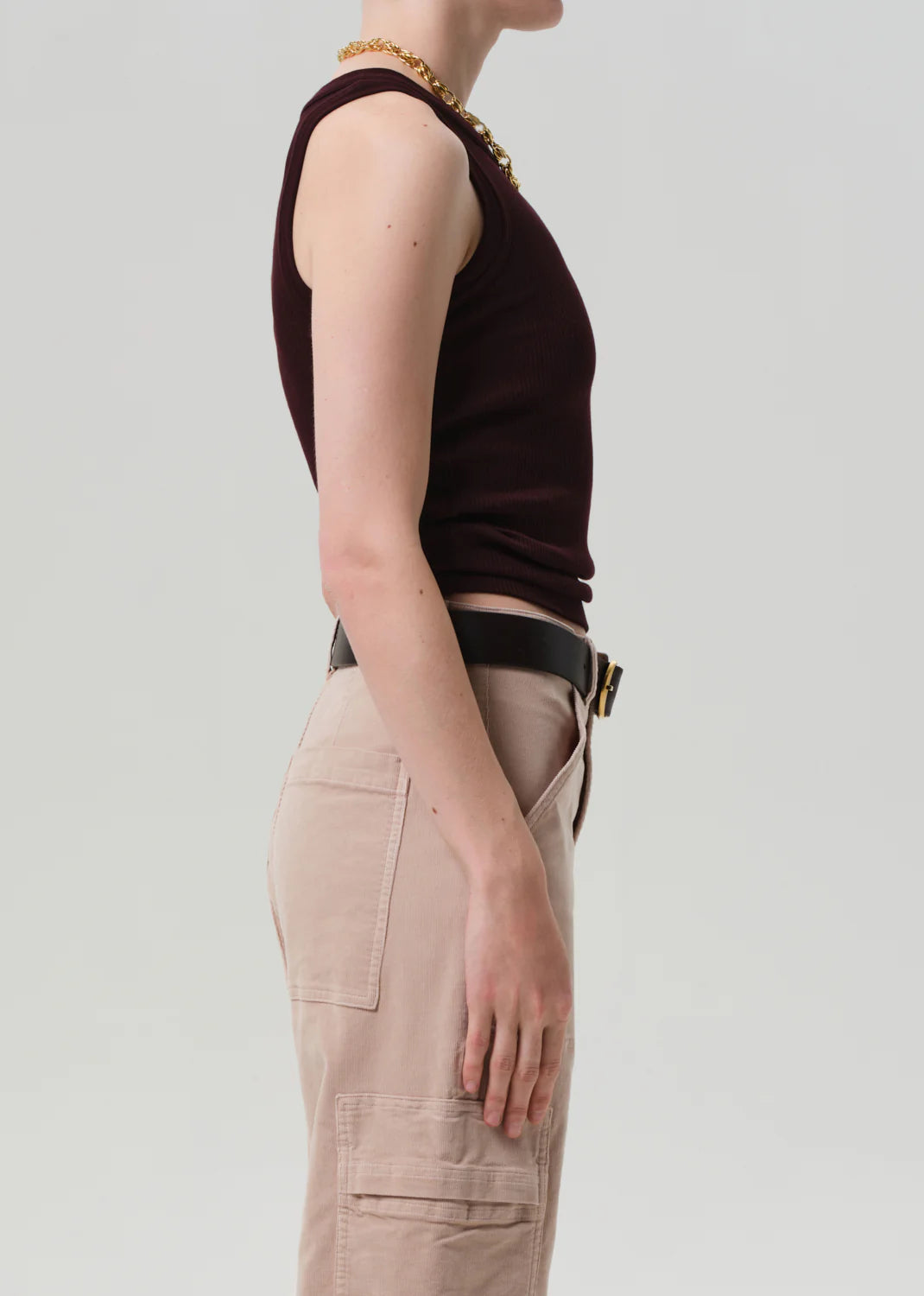 A person stands in profile against a plain background, wearing the Isabel Rib Tank F25 by Citizens Of Humanity/AGOLDE, paired with beige cargo pants featuring visible pockets and accessorized with a gold chain necklace.