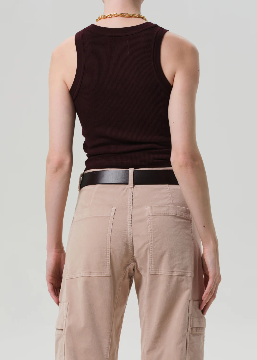 A person faces away from the camera wearing the Citizens Of Humanity/AGOLDE Isabel Rib Tank F25 in dark brown, styled with a black belt and light beige cargo pants. The background is plain and light.