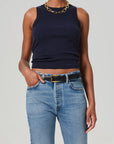 Wearing the Isabel Rib Tank by Citizens Of Humanity/AGOLDE, someone pairs this sleeveless black ribbed racerback with a chunky gold chain necklace, blue jeans with a black belt, and casually places one hand in their pocket.
