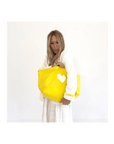 Yellow KR Imperfect Heart Tote by Kerri Rosenthal with a leather heart charm, styled by woman in white.