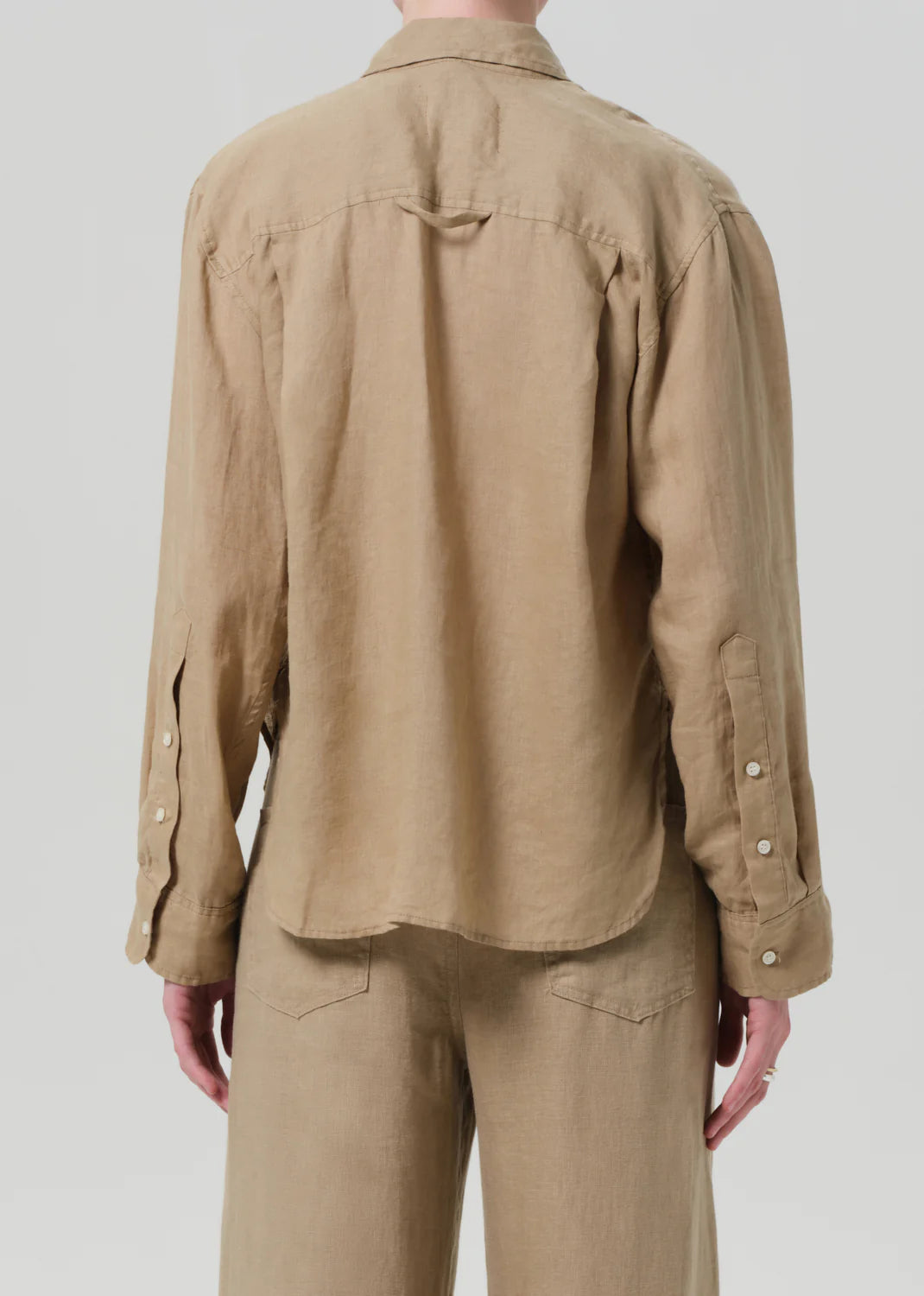 A person is seen from the back wearing the Kayla Shirt F25 by Citizens Of Humanity/AGOLDE, a lightweight, loose-fitting linen shirt in light brown, paired with matching pants and set against a plain light background.