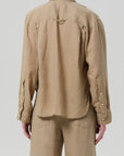 A person is seen from the back wearing the Kayla Shirt F25 by Citizens Of Humanity/AGOLDE, a lightweight, loose-fitting linen shirt in light brown, paired with matching pants and set against a plain light background.