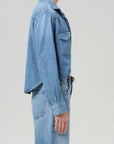 A person wearing the Citizens Of Humanity/AGOLDE cropped western shirt with flap chest pockets and a matching skirt is shown in profile against a light gray background, with their head partially out of frame.