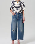 Dressed in the Citizens Of Humanity/AGOLDE Goldie Tee, an oversized black and white striped rib cotton top tucked into high-waisted wide-leg distressed jeans, the person completes their look with black strappy heels and a gold necklace against a plain gray background.