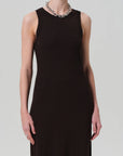 A person wears the Isabel Tank Dress by Citizens Of Humanity/AGOLDE—a sleeveless, fitted black ribbed dress—with a chunky silver chain necklace. Their hand rests by their side, and the plain light background highlights the cropped composition.