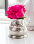 A vibrant pink rose rests in Faire’s Vintage 1815 Pitcher, a small, handmade piece with engraved Italian detailing, gleaming softly on a white surface by the window.
