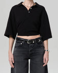 Someone is wearing the lowen polo shirt by Citizens Of Humanity/AGOLDE, paired with black high-waisted jeans, a black belt, and silver jewelry against a plain light background.