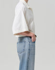 A person stands in profile with one hand in the pocket of light blue jeans, wearing the Citizens Of Humanity/AGOLDE Lowen Polo Shirt in breathable pique fabric, set against a plain light background.