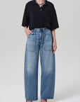 Model wears the Citizens Of Humanity/AGOLDE Lowen Polo Shirt—oversized, black, textured knit cotton—tucked into high-waisted, wide-leg blue jeans with large front pockets; paired with black pointed-toe heels against a plain light background.