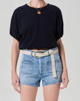Wearing the Citizens Of Humanity/AGOLDE gia bubble tee tucked into high-waisted light blue denim shorts with front pockets, styled with a wide white belt, gold necklace, and ring against a plain light background.