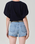 A person is shown from the back wearing the gia bubble tee by Citizens Of Humanity/AGOLDE, paired with light blue denim shorts with rolled cuffs, a beige belt, and a gold necklace. The background is plain light gray.