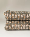 A close-up of two folded Faire Blossom Block Print Quilts with a white and orange floral pattern, stacked against a plain, light background.
