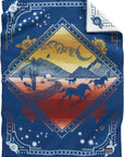 The Jacquard Whipstitch Muchacho by Pendleton/Babbitt's Wholesale is a pure virgin wool woven blanket featuring a desert scene with horses, cacti, mountains, and clouds in a diamond frame, plus blue, white, orange, and yellow floral/star borders.