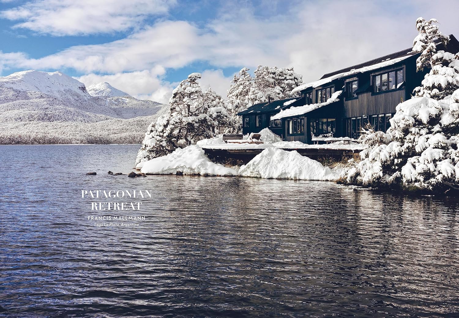 A modern dark cabin by a snowy lake, inspired by mountain houses and curated interiors, is nestled among trees and distant mountains; text reads "Mountain House by Random House.