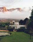 A modern white villa inspired by mountain houses rests among gardens and peaks, shrouded in drifting clouds. Text overlay: "Mountain House" by Random House, with interior design by expert Nina Freudenberger.