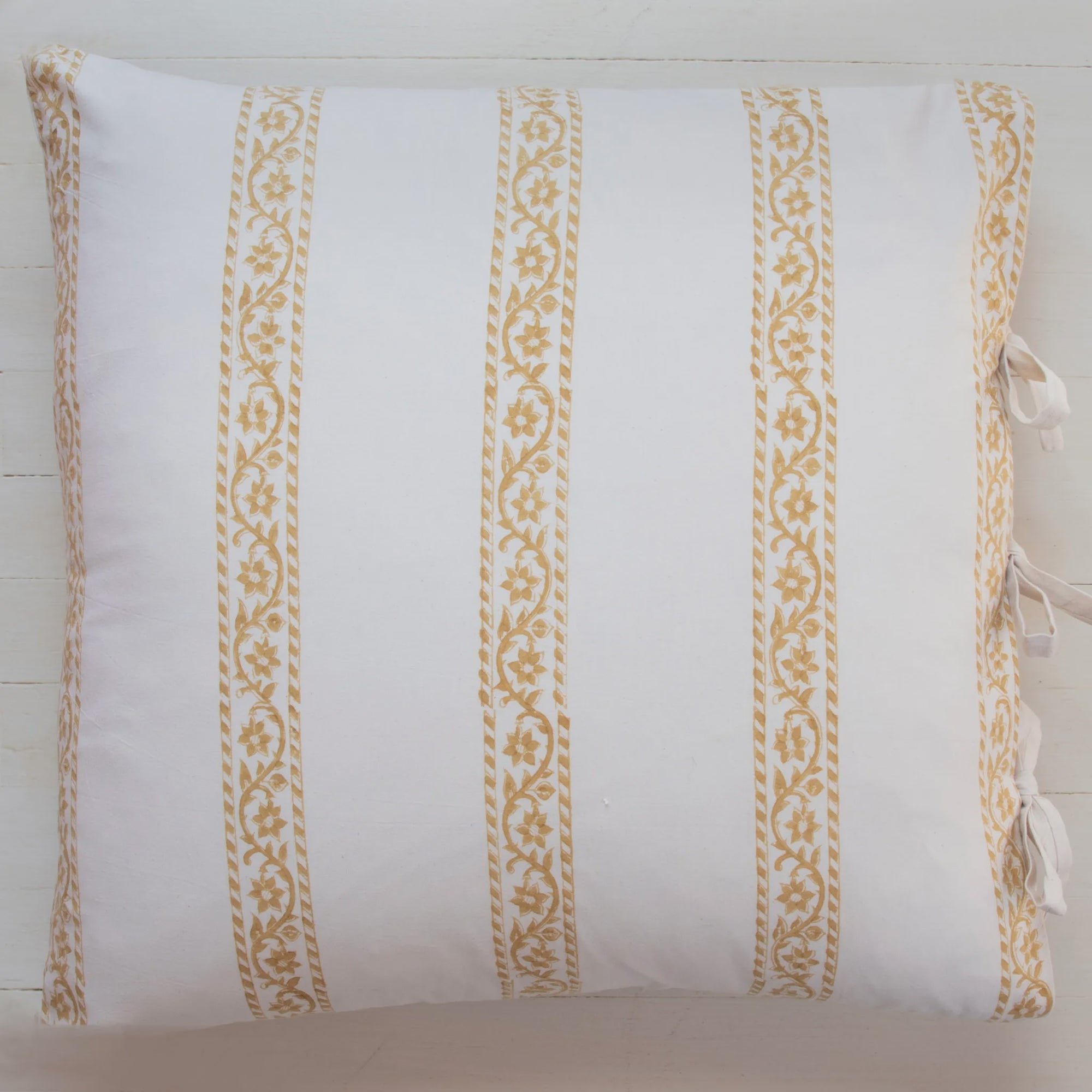 A Les Indiennes Sandrine Deco Sham Only 22x22 featuring vertical gold patterned stripes and small tied ribbons at the corners, displayed against a light wooden background in a Scottsdale Arizona bungalow.