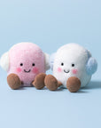 Two plush Amuseables Toastie Pink and White Marshmallows by Jelly Cat Inc., with rosy cheeks, brown corduroy feet, and matching earmuffs, sit side by side on a light blue background—perfect winter companions.