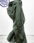 An olive green CanyonKid Tanks Flap/Snap Homestud jacket by Free City (sparrow, LLC) with metallic studs hangs on a white hook. A blue circular stamp and "art+commerce" logo are shown in the corners against a plain background.