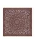 The Silk Bandana by The Great Inc. is a brown silk accessory with a classic paisley pattern and white decorative edges and center, offering an elegant vintage-inspired style.