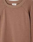 A close-up of the Atubay Sweatshirt by American Vintage shows its brown, oversized raglan design with a white tag inside the collar. The soft knit fabric adds to this women’s sweatshirt’s cozy appeal.
