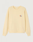 The Atubay Sweatshirt by American Vintage is a light yellow women's crewneck fleece with long sleeves, featuring a small, colorful graphic and text on the left chest accented by red, blue, and green elements. Displayed on a plain background.