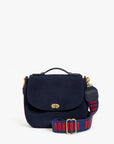 The Clare Vivier Crossbody Strap S25 is a navy blue suede handbag with a top handle, gold clasp, and an adjustable cotton strap featuring "BONJOUR" in bold red letters.