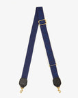 The Clare Vivier Adjustable Crossbody Strap features blue cotton webbing, gold-tone clasps, black leather trim, and raised “DÉJÀ VU” lettering in blue.