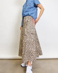 A woman stands against a plain background wearing the Aquarius Cocktail Le Cargo Skirt, styled with a short-sleeved denim shirt and white sneakers. Her face is partially out of frame.