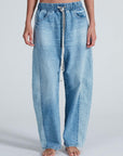 A person stands barefoot, hands by their sides, wearing the ASKK Cancun Pant—relaxed fit, light blue Japanese denim with an elastic waistband and drawstring—against a plain light background.