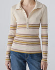 A person wears the AMO Denim Desiree Tee—a cream-colored ribbed top with multicolored horizontal stripes and a classic collar—paired with blue jeans, standing against a plain light background.