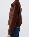 Model wearing the AMO Denim Isabelle Jacket in brown wool with flap pockets and buttoned cuffs, paired with blue jeans, shown from the side against a plain light background for a flattering silhouette.