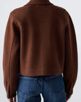Model shown from the back in the AMO Denim Isabelle Jacket, a brown, collared, long-sleeve cropped trucker with large cuffs, paired with blue jeans against a plain light background for a flattering silhouette.