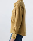 A person wearing the AMO Denim Jenn Shirt, a loose-fitting tan corduroy top with a western-style chest pocket, paired with blue jeans and shown from the side against a plain light background.